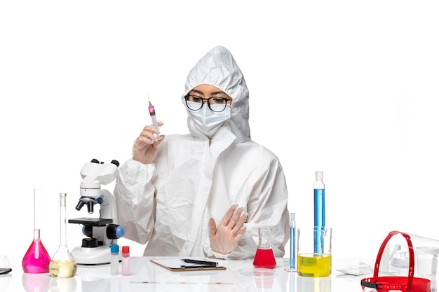 Женщина-химик в специальном защитном костюме, работающая с инъекциями на белом столе, химическая лаборатория covid, вид спереди