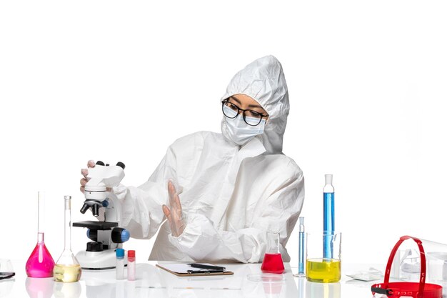 Front view female chemist in special protective suit working with microscope on a white background covid chemistry virus lab