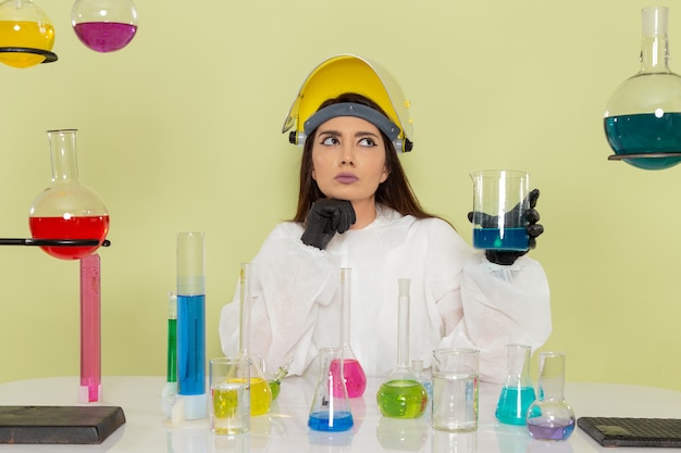 Front view female chemist in special protective suit working with solutions on the green surface