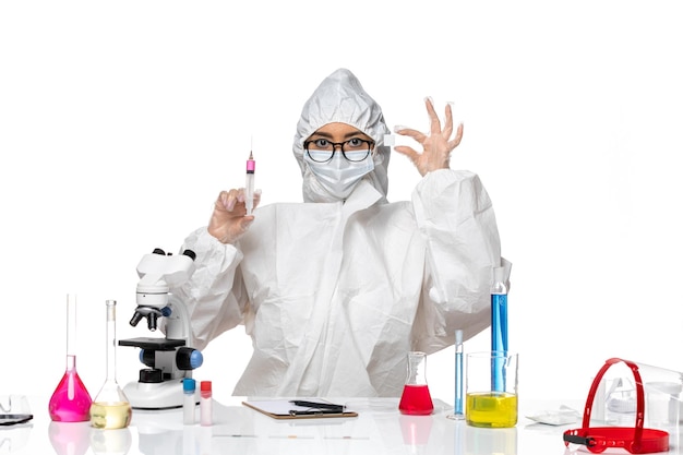 Front view female chemist in special protective suit working with solutions and injection on light white background covid chemistry virus lab