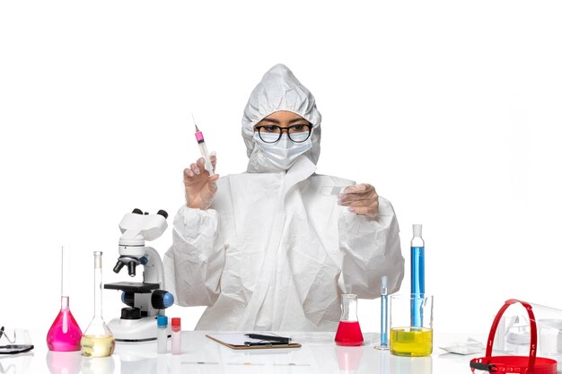 特別な防護服を着た女性化学者の正面図白い背景のcovid化学ウイルスラボでソリューションと注射を使用しています