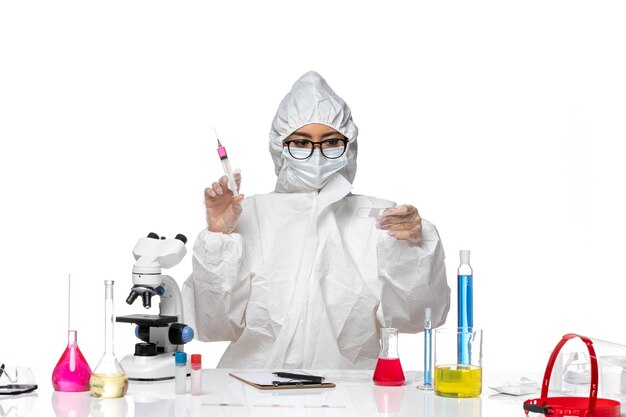 Front view female chemist in special protective suit working with solutions and injection on a white background covid chemistry virus lab