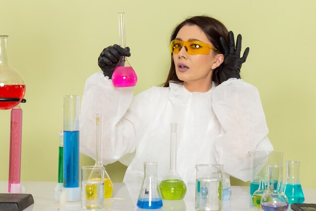 Front view female chemist in special protective suit working with solutions on the light-green surface