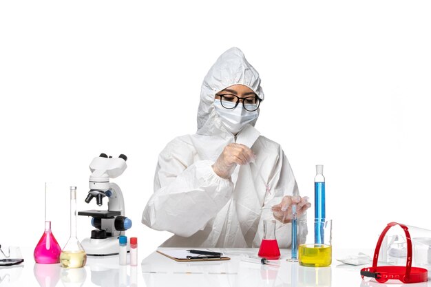 Front view female chemist in special protective suit working with solutions on light white background virus covid chemistry lab