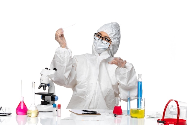 Front view female chemist in special protective suit working with solutions on a light white desk virus covid chemistry lab