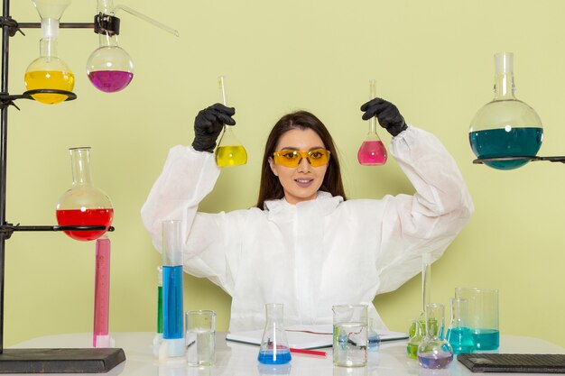 Front view female chemist in special protective suit working with solutions and smiling on green surface