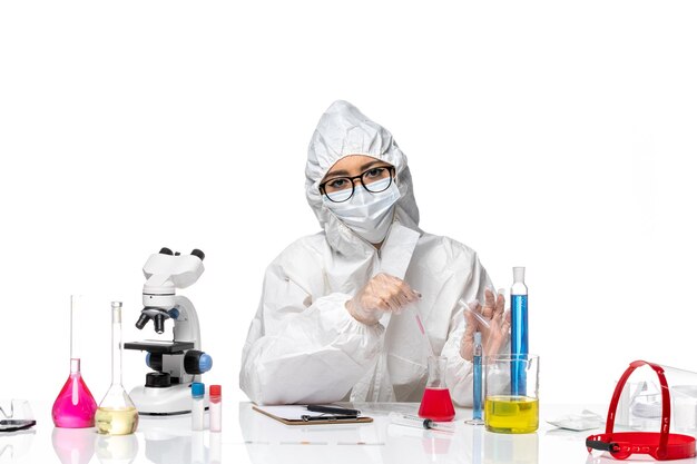 Front view female chemist in special protective suit working with solutions on white desk health virus covid chemistry