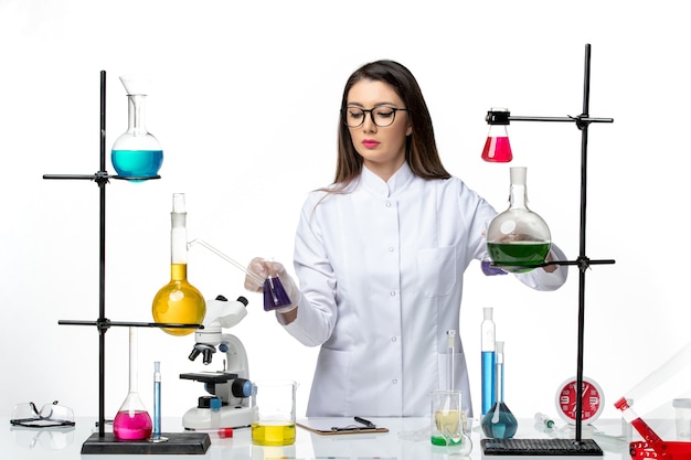 Вид спереди женщина-химик в стерильном медицинском костюме, стоящая вокруг стола с растворами на светлом белом фоне, вирусное заболевание, covid - пандемия науки