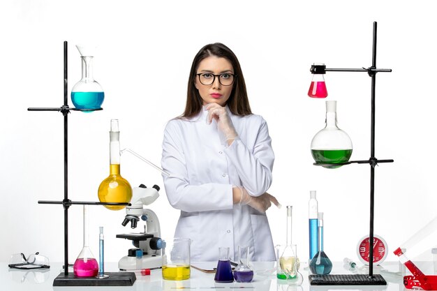 Вид спереди женщина-химик в стерильном медицинском костюме, стоящая за столом с растворами на белом фоне, вирусное заболевание, лаборатория covid, пандемия науки