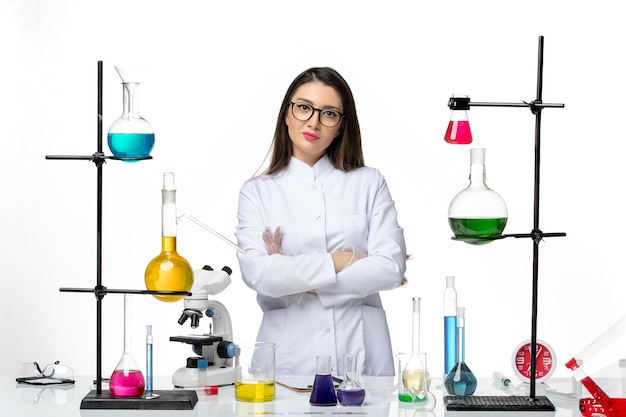 Front view female chemist in sterile medical suit standing around table with solutions on white background virus disease covid- lab science