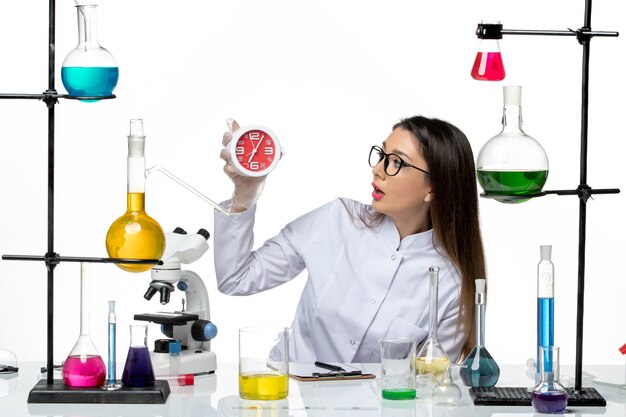 Front view female chemist in white medical suit holding clocks on white background science virus lab covid pandemic