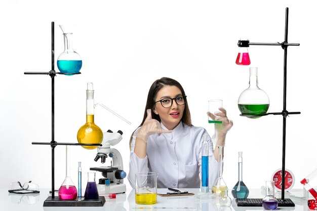 Front view female chemist in white medical suit holding flask with solution on light white background science virus covid pandemic lab