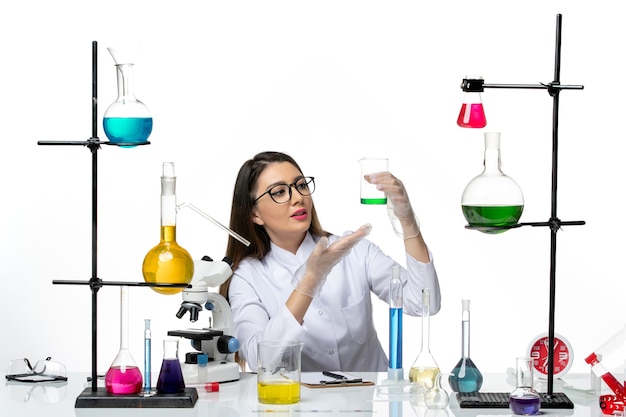 Front view female chemist in white medical suit holding flask with solution on white background lab science virus covid pandemic
