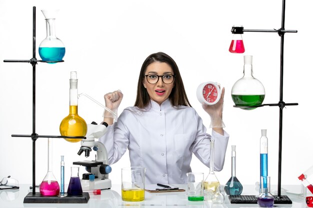 Front view female chemist in white medical suit holding red clocks on white background science virus lab covid- pandemic