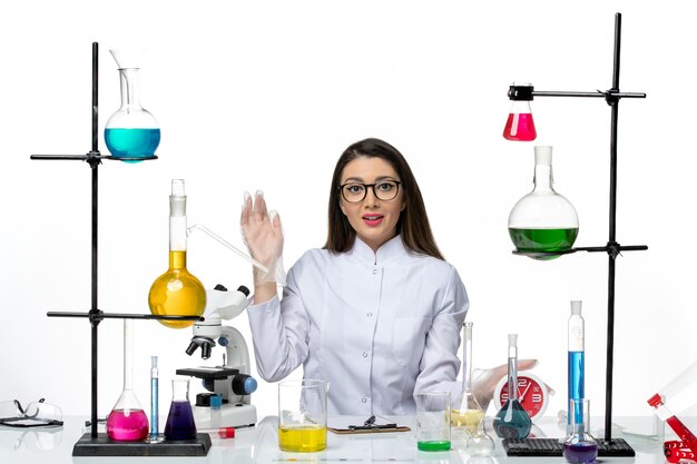 Front view female chemist in white medical suit just sitting with solutions on light white background science covid- lab pandemic virus