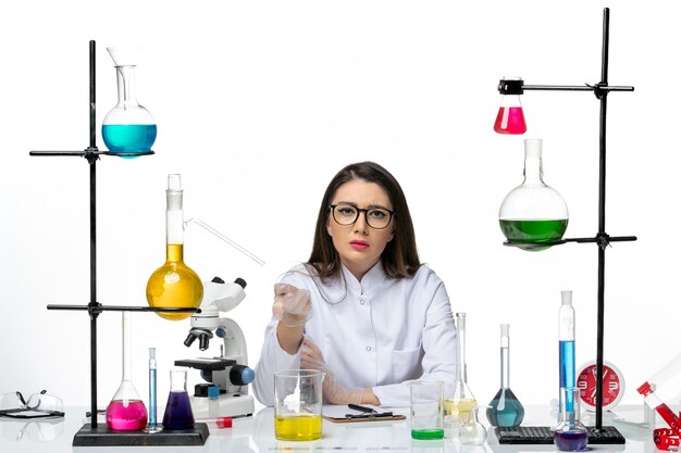 Front view female chemist in white medical suit just sitting with solutions on light-white background science virus covid- pandemic lab