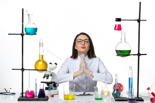 Front view female chemist in white medical suit just sitting with solutions on the white background science covid- lab pandemic virus