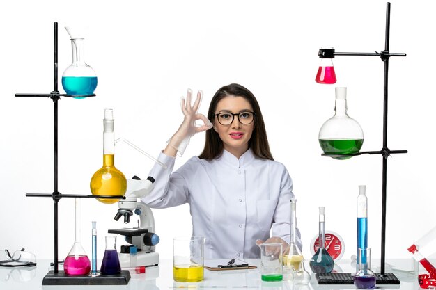 Front view female chemist in white medical suit just sitting with solutions on white background science covid pandemic lab virus