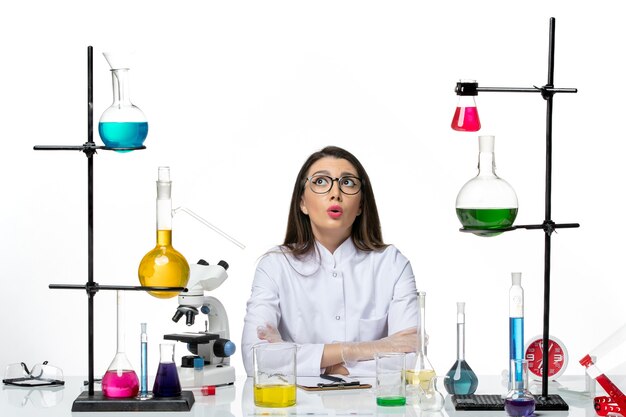 Вид спереди женщина-химик в белом медицинском костюме, просто сидящая с растворами на белом фоне, научный вирус covid - пандемическая лаборатория
