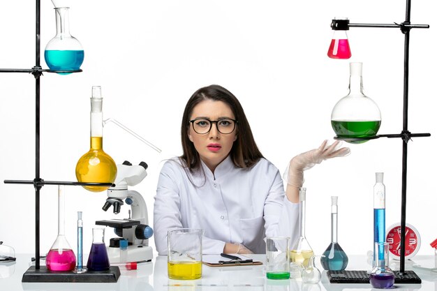 Front view female chemist in white medical suit just sitting with solutions on white background science virus covid- pandemic lab