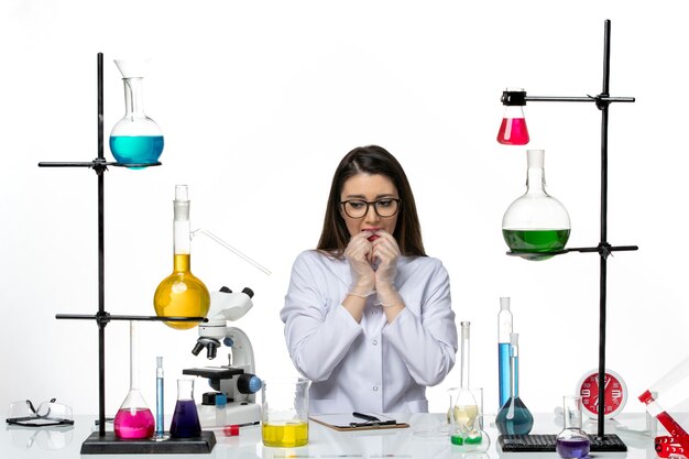 Front view female chemist in white medical suit sitting and feeling nervous on white background lab science virus covid pandemic