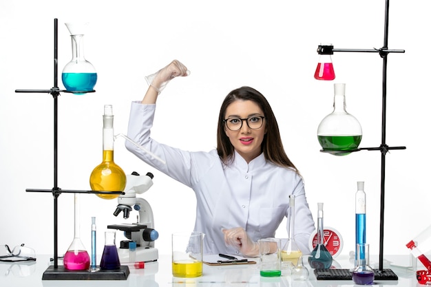 Вид спереди женщина-химик в белом медицинском костюме, сидящая с разными растворами на белом фоне, научный вирус, пандемическая лаборатория covid
