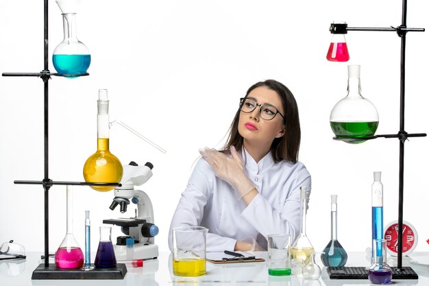 Вид спереди женщина-химик в белом медицинском костюме, сидящая с растворами на белом фоне, научный вирус covid - пандемическая лаборатория