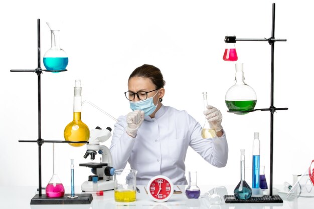 Front view female chemist in white medical suit with mask holding solution coughing on white background chemist lab virus covid- splash