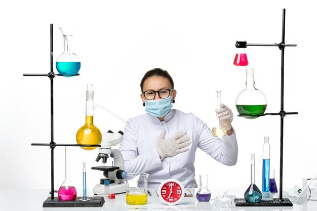 Front view female chemist in white medical suit with mask holding solution on the light white background chemist lab virus covid- splash