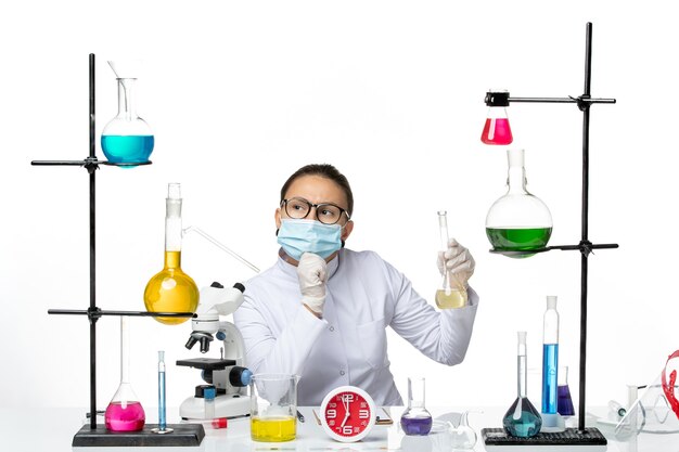 Front view female chemist in white medical suit with mask holding solution thinking on white background chemist lab virus covid splash