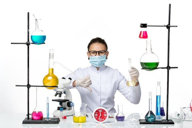 Вид спереди женщина-химик в белом медицинском костюме с маской, держащей раствор на белом фоне, всплеск вируса covid из лаборатории химика