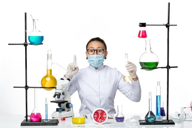 Вид спереди женщина-химик в белом медицинском костюме с маской, держащей раствор на белом фоне, всплеск вируса covid из лаборатории химика