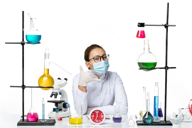 Вид спереди женщина-химик в белом медицинском костюме с маской, сидящая с растворами на белом фоне, химическая лаборатория вируса covid- splash