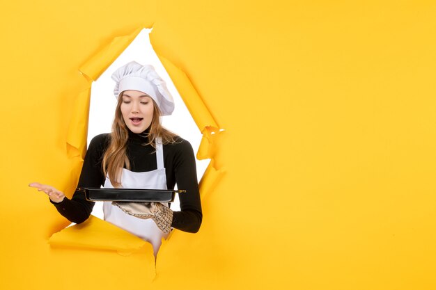 Front view female confectioner holding black pan with biscuits on yellow photo emotion sun food kitchen cuisine color job