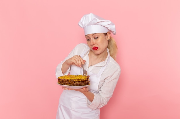 Free photo front view female confectioner in white wear holding delicious pastries designing it on the pink wall