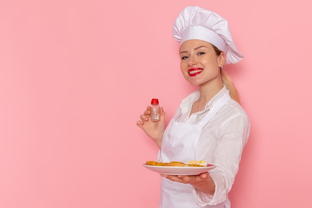 Front view female confectioner in white wear holding plate with food on the pink wall cook job kitchen cuisine food