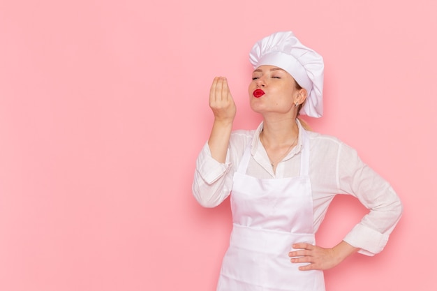 Pasticcere femminile di vista frontale nell'usura bianca che posa sul lavoro di lavoro della pasticceria dolce della pasticceria del cuoco della parete rosa