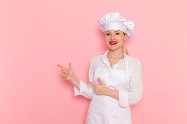 ピンクの壁に笑みを浮かべてポーズをとって白い服を着た正面図の女性菓子屋料理菓子甘いペストリーの仕事