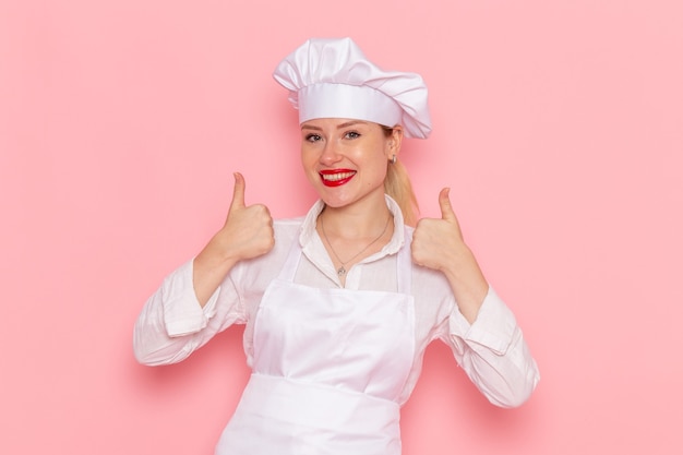 Foto gratuita pasticcere femminile di vista frontale nell'usura bianca che sorride e che posa sul lavoro rosa della pasticceria della pasticceria del cuoco della parete