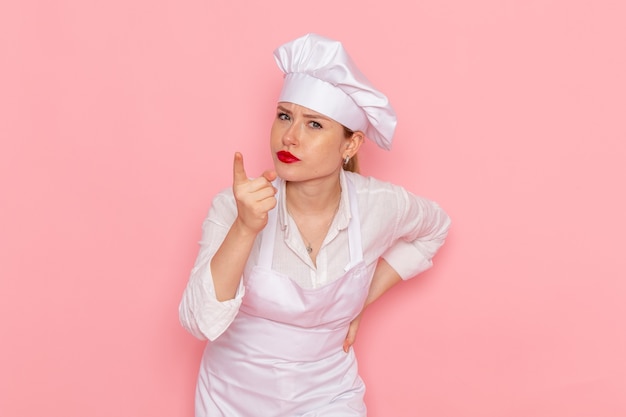 白い服を着た正面図の女性菓子屋は、淡いピンクのデスク菓子の甘いペストリーの仕事を脅かしています