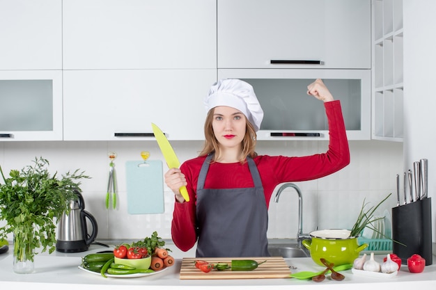 Женщина-повар, вид спереди в фартуке, показывает мышцу руки