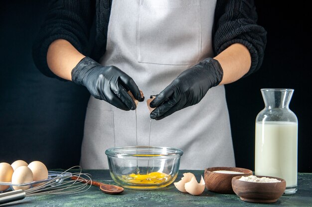 Вид спереди женщина-повар, разбивающая яйца для теста на темном тесте, пирог, пирог, работник пекарни, хоткейк, кухня, работа