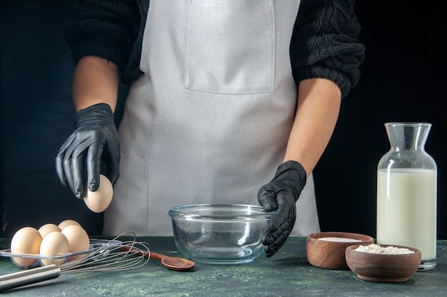 Front view female cook breaking eggs for dough on dark pastry job cake pies bakery worker cuisine