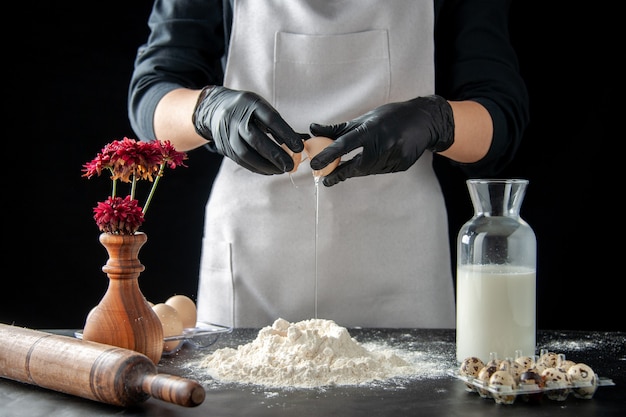 Front view female cook breaking eggs into flour on dark job pastry pie bakery bake cake biscuit dough