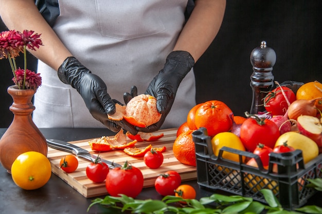 Вид спереди женщина-повар, чистящая мандарины на темноте, кулинария, салат, здоровая диета, овощная еда, еда, фрукты, работа