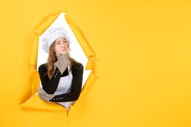 Front view female cook in cook gloves and white cook cap on yellow food color cuisine photo emotion kitchen job