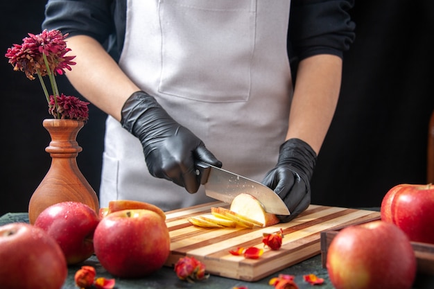 Вид спереди женщина-повар режет яблоки на темных овощах, диетическом салате, еде, напитке, фруктах