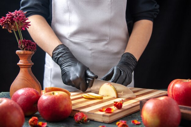 Вид спереди женщина-повар режет яблоки на темных овощах, диета, салат, еда, еда, экзотический напиток, фрукты
