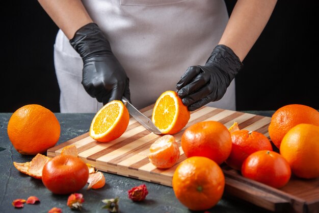 Front view female cook cutting orange on a dark salad health meal food job vegetable fresh drink fruit diet