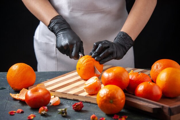 Вид спереди женщина-повар режет апельсин на темном салате здоровое питание еда работа овощной свежий напиток фруктовая диета